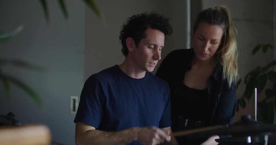 A woman teaches a man how to play the drums