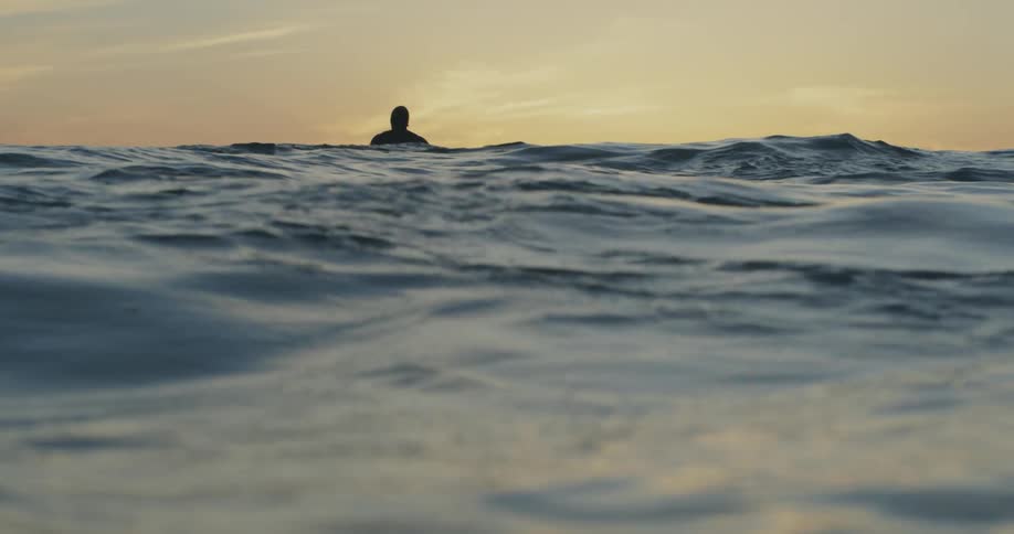 A man bobs in the ocean at sunset