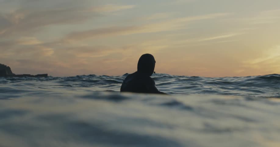 A man is swimming in the water off the coast as it waves and moves under a cloudy sky