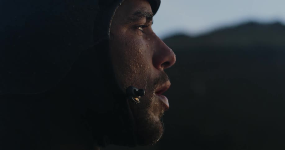 Water drops dot face of man wearing wet suit with promontory in the background
