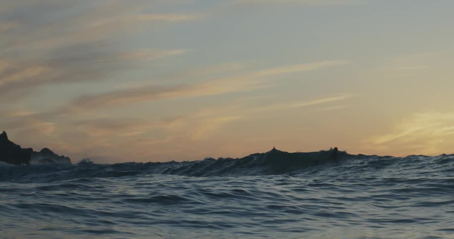 Sunlight reflects on splashing rough water waves as they roll in to shore and a person is swimming