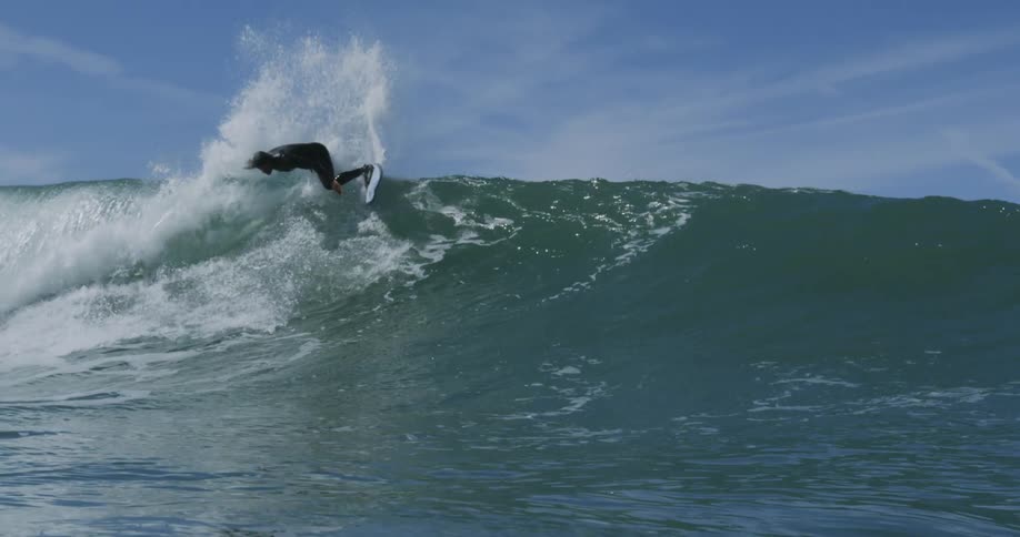 A large ocean wave as a man on a surf board rides down the wave