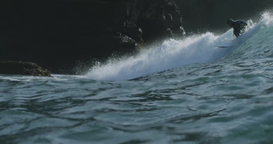 A surfer rides a big wave near the shore along side a cliff
