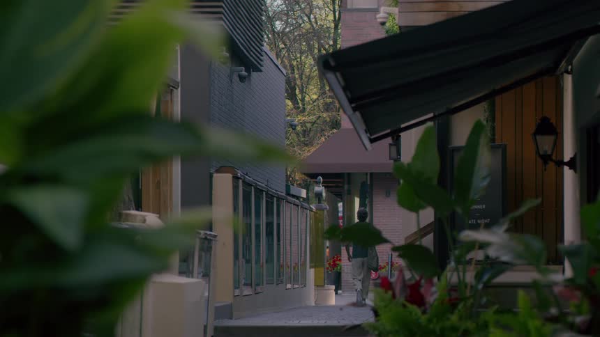 A man walks along a pathway that leads between a few buildings