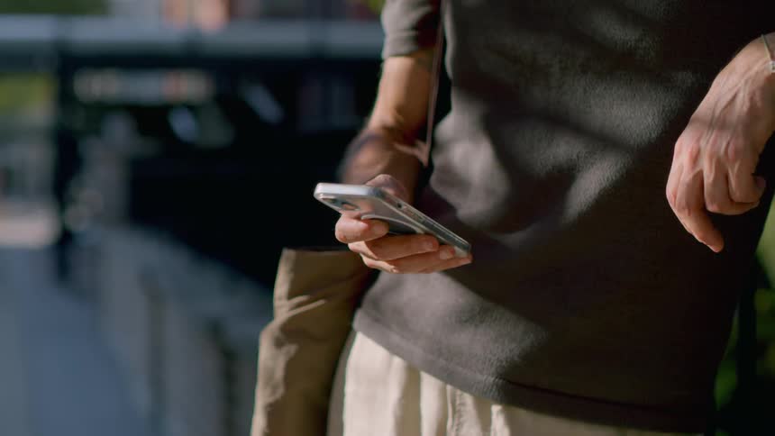 A man is standing outside holding his cell phone and scrolling with his thumb