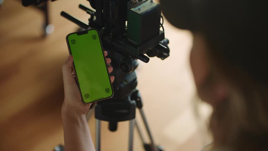Woman holds smartphone while standing in front of camera on tripod