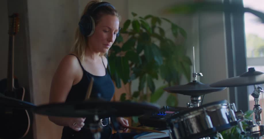 A woman playing a drum setwith headphones on nodding her head and bobbing to the music