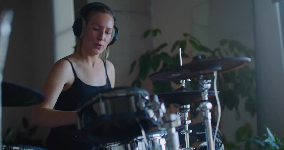 Woman wears headphones and sits and drums