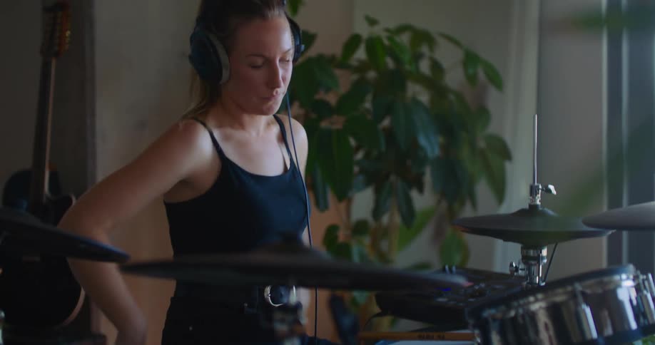 Woman with black top and ponytail wears headphones and play the drums