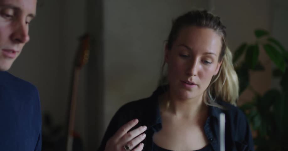 Blonde woman with ponytail black top teaches man how to play drums