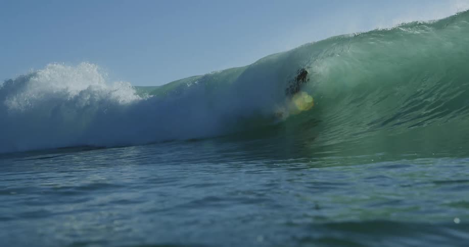 Surfer stands on surfboard and rides along wave and through its barrel