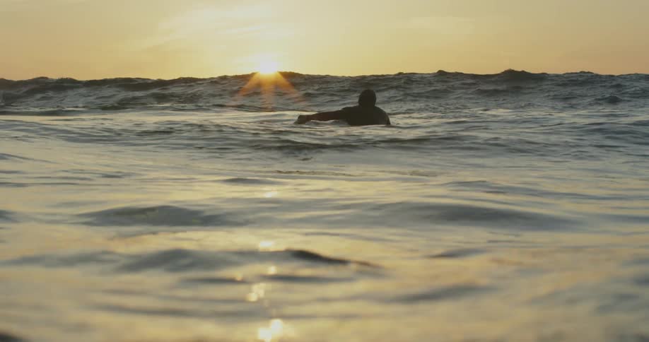 A silhouette of a man floating in the ocean as the sun is setting on the horizon