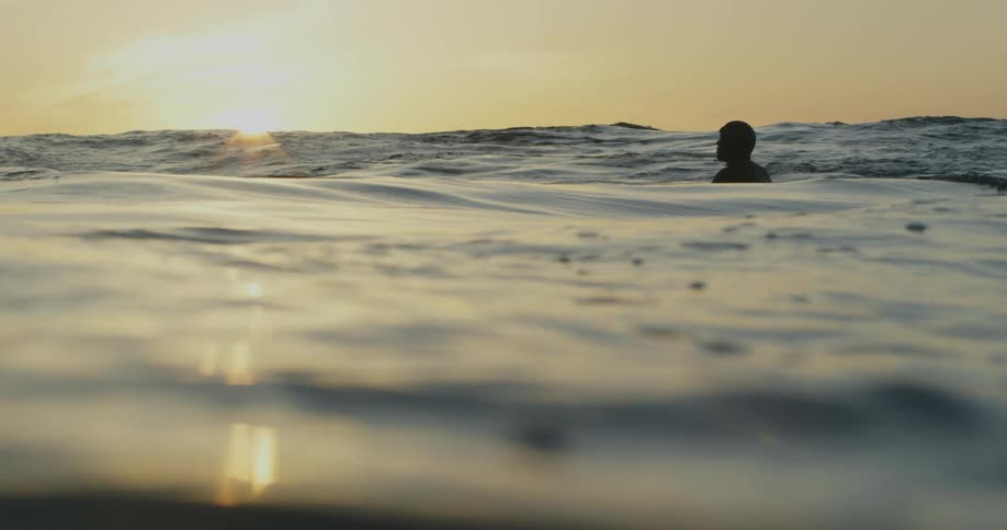 A man bobbing in the wavy ocean as the sun reflects off the surface