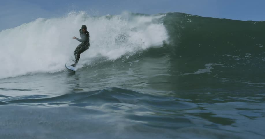 A man in a black wet suit on a surf board riding a large wave on the ocean