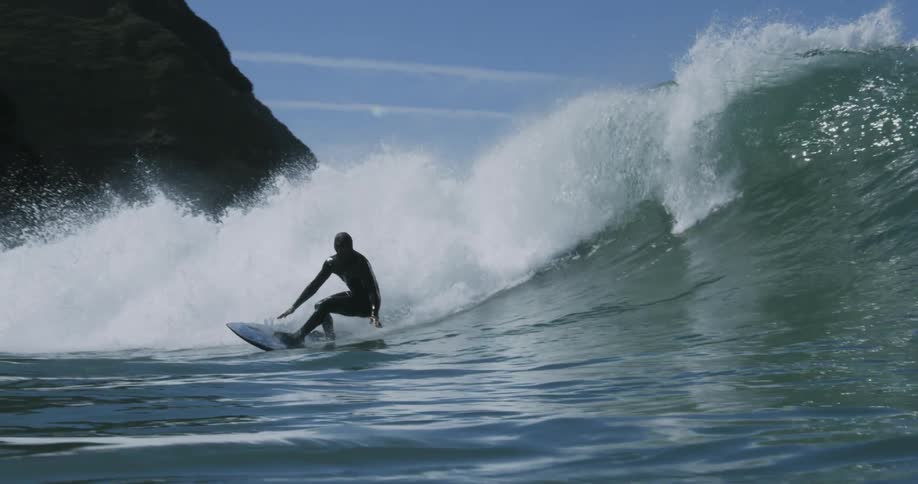 A surfer riding atop a massive wave is captured doing so in slow motion