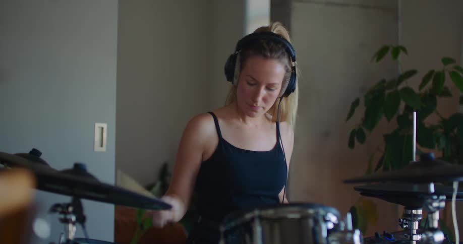 A woman wears headphones while playing the drums