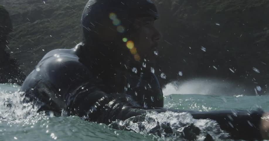Surfer wearing wet suit paddles away from shore on surfboard