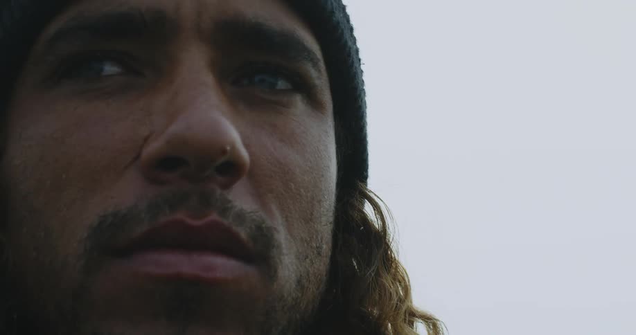 A man with long curly hair looks around at his surroundings on a gray day