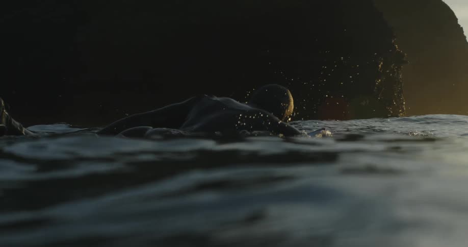 Man in wetsuit swims on surfboard off the coast