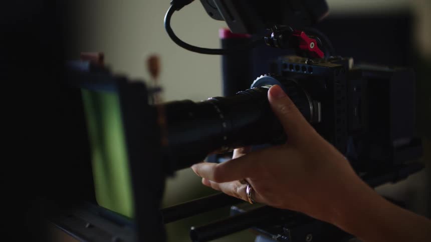 A woman is adjusting the lens of a camera on a tripod as she stands behind it