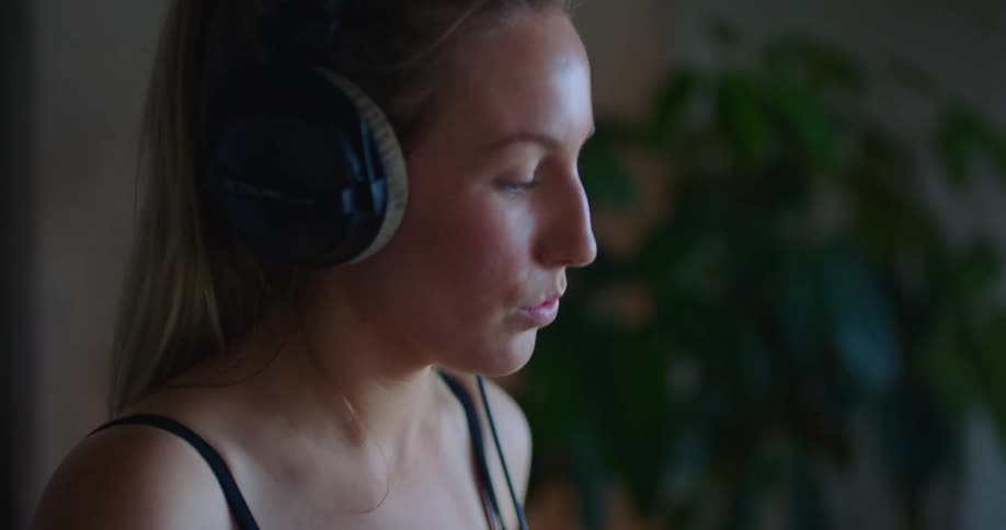 Blonde woman with ponytail black top and headphones play drums in room