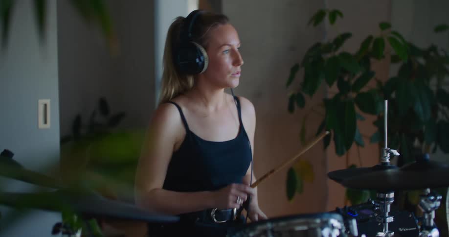 A blonde woman is playing the drums indoors while wearing headphones
