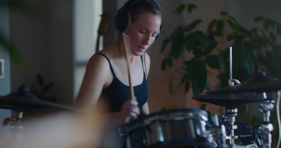 Blonde woman with ponytail black top and headphones play drums in room