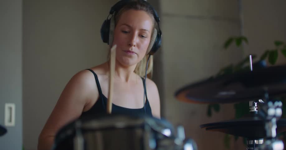 Blonde woman with ponytail headphones and black top play drums