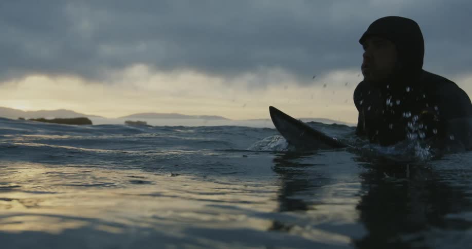A man is lying on his surfboard as he paddles with his arms across the water