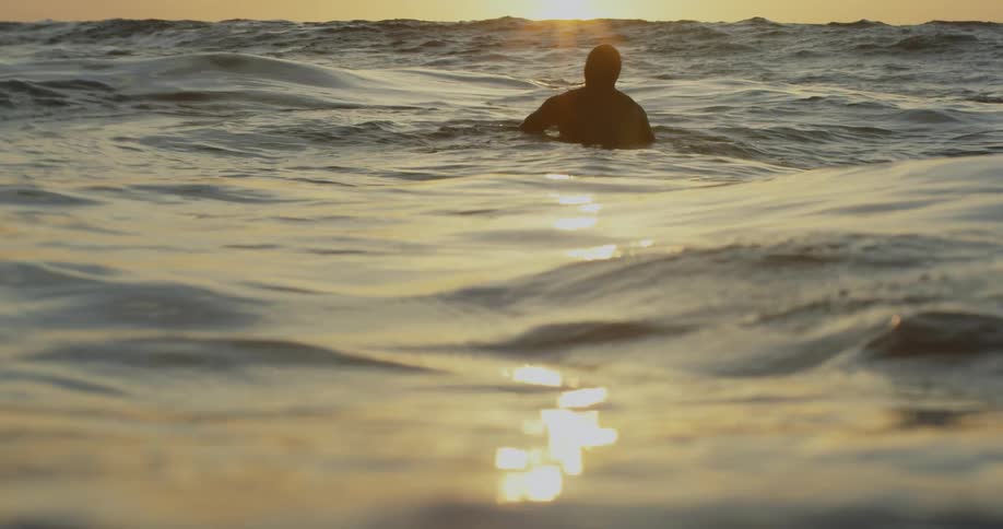A person wading in rough waters looking out over the sun reflecting off the horizon