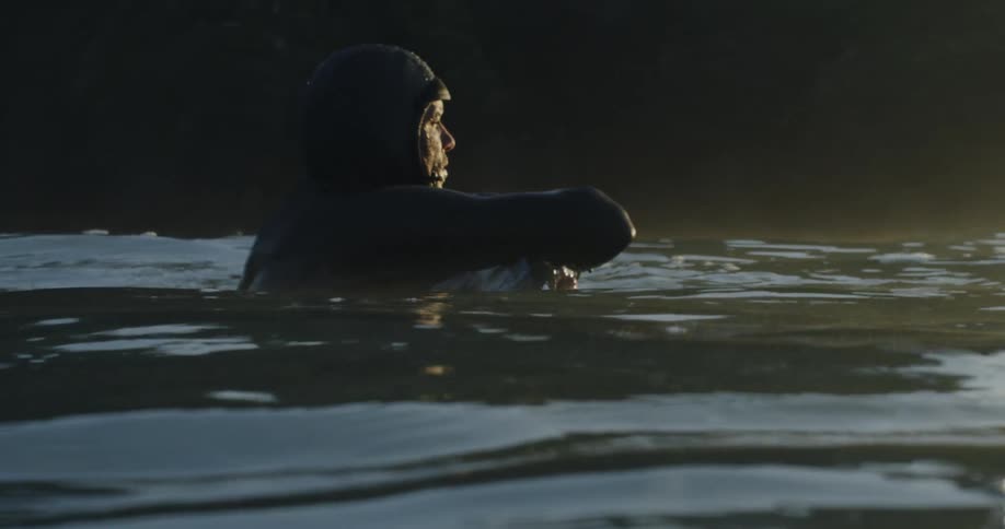 A man sits with his arms wrapped around his knees in the ocean