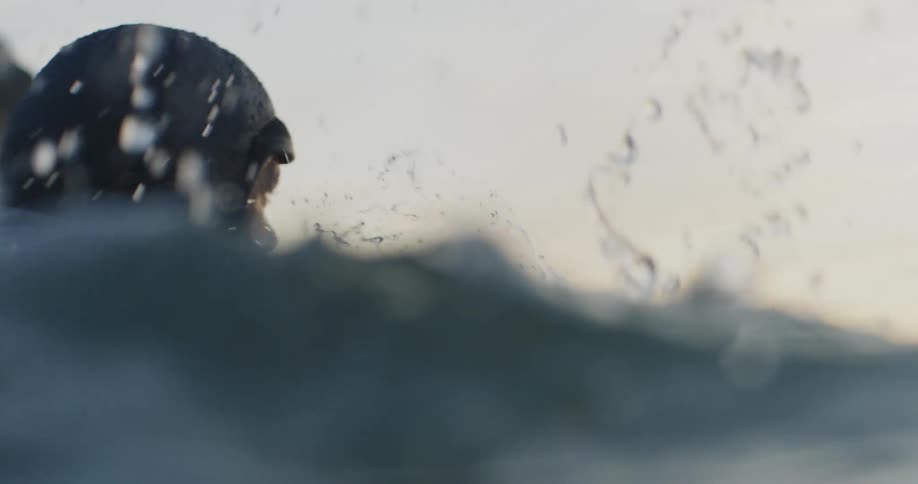 Man with wet suit on surfboard in ocean paddling into an incoming wave