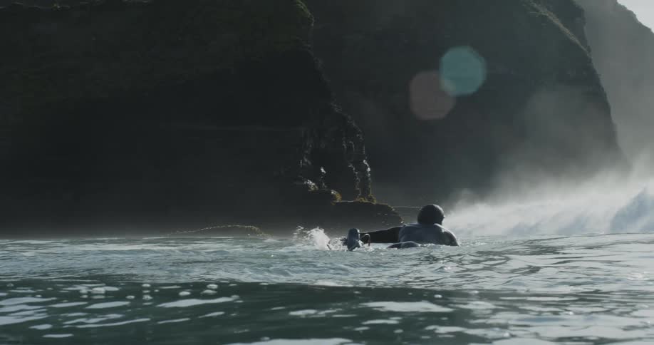 A man paddles on his surfboard toward a cave in the ocean