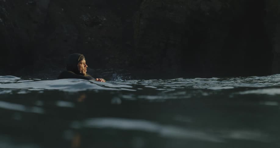 A man wearing a wetsuit is leaning on a surfboard as he floats on the water