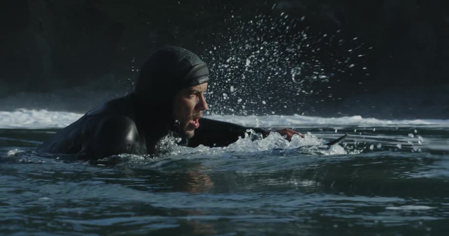 Man in wetsuit swims on surfboard off the coast