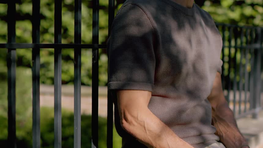 Man sitting outside of iron entry gate to residence during the day