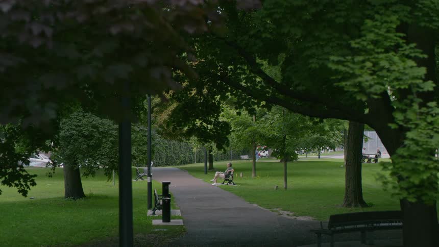 A man is sitting on a park bench as someone walks in the distance