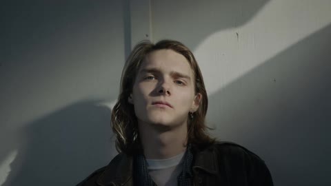 Man stands near a white wall and stares forward
