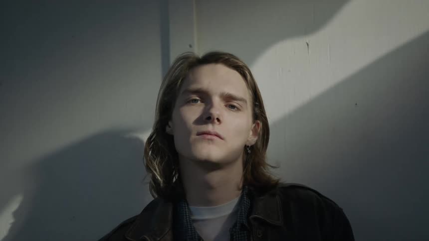 Man stands near a white wall and stares forward