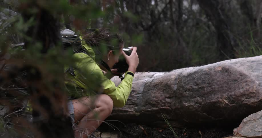 A female photographer crouching behind a rock taking photos