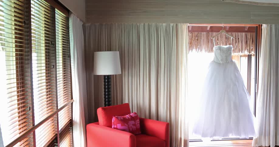 A white wedding dress hangs in front of the window