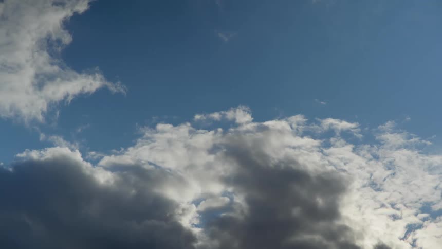 Clouds slowly moving across the sky as the sunlight reflects behind them against a blue sky