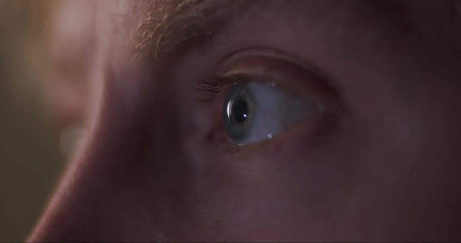 Extreme closeup of a mans grey colored eye staring at a tv screen making small movements following its focus
