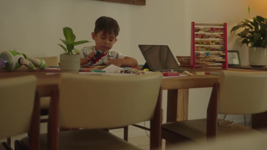 Boy with white shirt plays with toys at the table in the living room