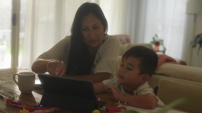 Mother and son sits at table using tablet in the living room