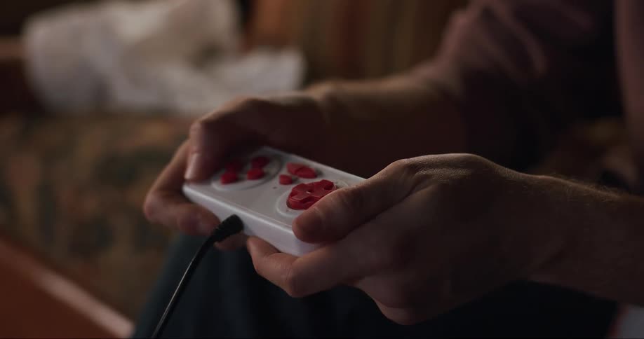 Man sitting on couch grabs game controller and proceeds to play using alternating thumb movementse