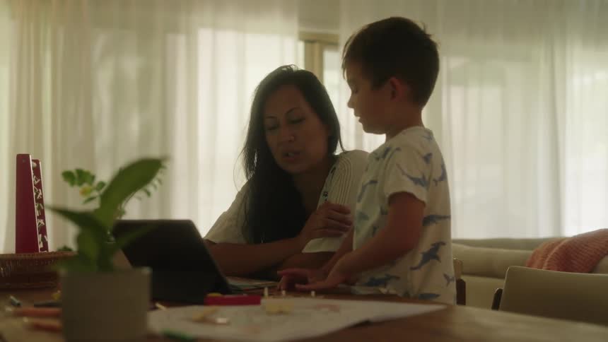 Mother and son at home maybe home school sitting at the table and working on a laptop and interacting