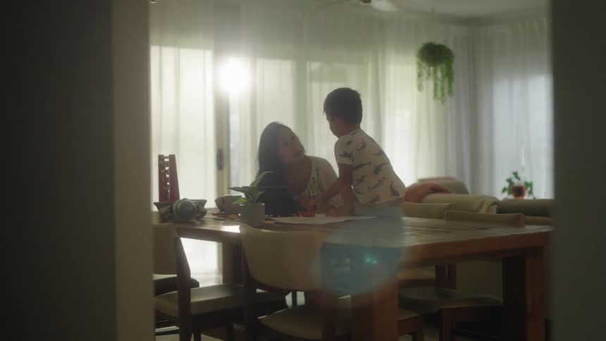 Mother and son sitting at table talk to each other in the living room at home