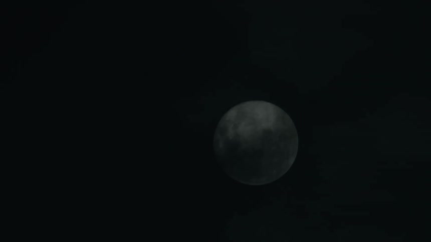 Clouds pass in front of a full moon in a starless night sky