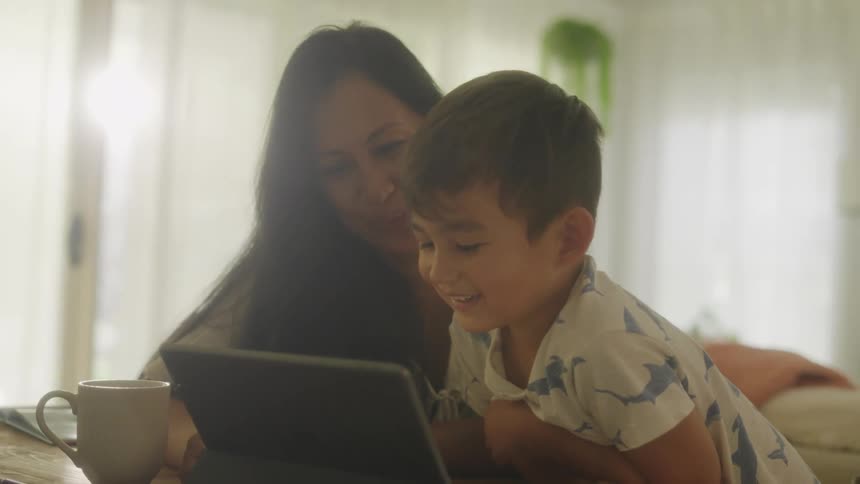 Mother and son smile while watching laptop screen at table at home